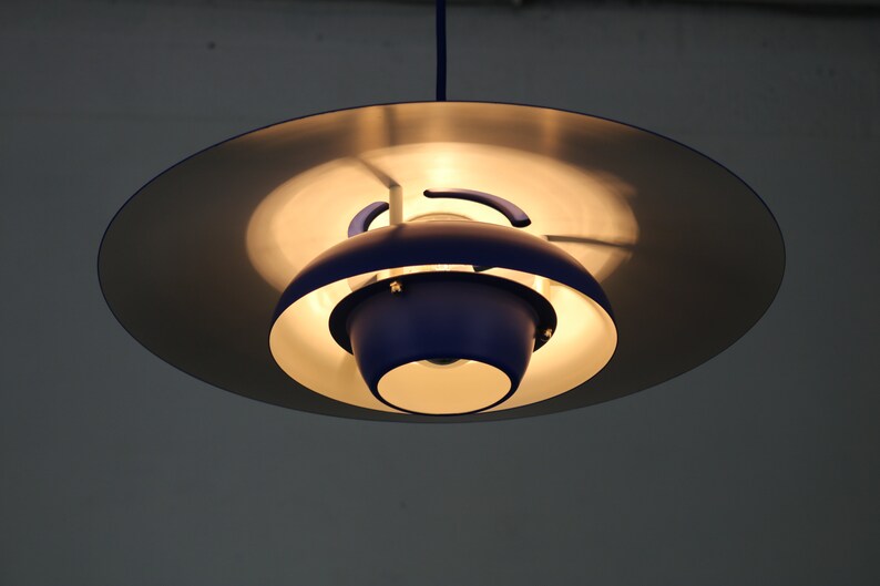 Op de afbeelding: Een blauwe en zilveren hanglamp met een ronde, schotelvormige kap.