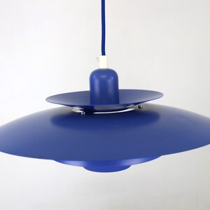 Op de afbeelding: Een blauwe hanglamp met een schotelvormige kap. De lamp heeft een eenvoudig ontwerp met &eacute;&eacute;n lamp.