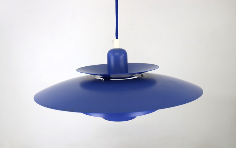 Op de afbeelding: Een blauwe hanglamp met een schotelvormige kap. De lamp heeft een eenvoudig ontwerp met &eacute;&eacute;n lamp.