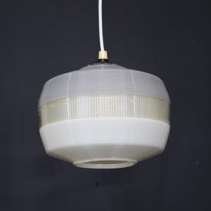 May include: A white pendant light with a ribbed glass shade. The shade has a horizontal band of smaller squares.