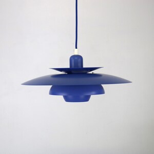 Op de afbeelding: Een blauwe hanglamp met een gelaagd, schotelvormig ontwerp. De lamp hangt aan een blauw snoer.