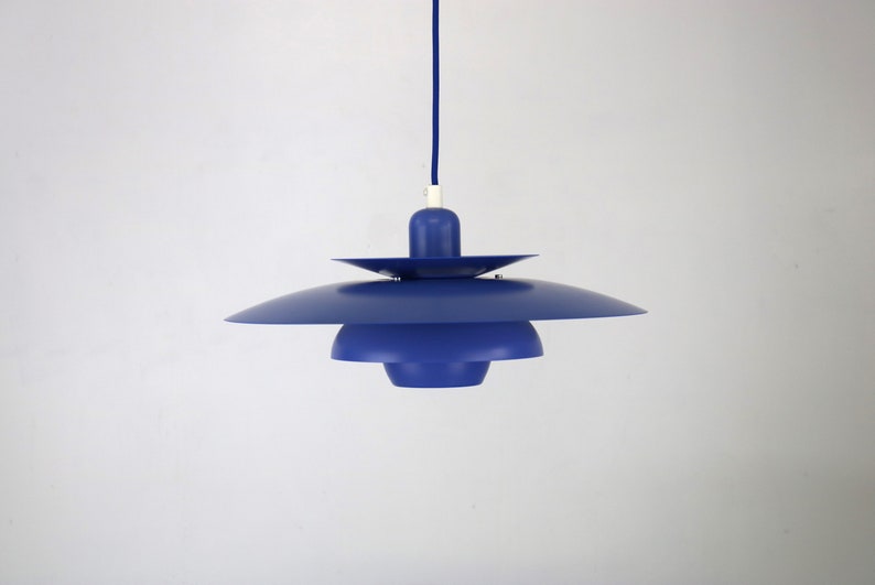 Op de afbeelding: Een blauwe hanglamp met een gelaagd, schotelvormig ontwerp. De lamp hangt aan een blauw snoer.