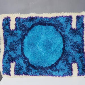 May include: A blue and purple shag rug with a white border. The rug has a circular design in the center.