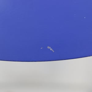 Puede incluir: Primer plano de una secci&oacute;n de un objeto azul brillante. El objeto tiene una superficie lisa con algunas peque&ntilde;as imperfecciones. El borde inferior del objeto es curvo. El fondo es de color gris claro.