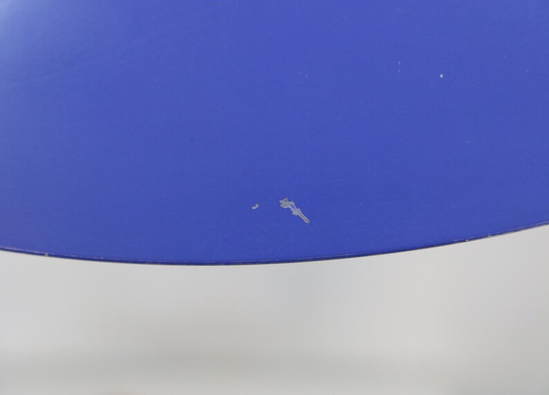 Puede incluir: Primer plano de una secci&oacute;n de un objeto azul brillante. El objeto tiene una superficie lisa con algunas peque&ntilde;as imperfecciones. El borde inferior del objeto es curvo. El fondo es de color gris claro.