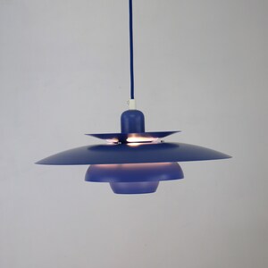 Op de afbeelding: Een blauwe hanglamp met een meerlaags kap. De lamp hangt aan een wit plafond.