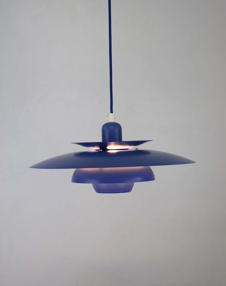 Op de afbeelding: Een blauwe hanglamp met een meerlaags kap. De lamp hangt aan een wit plafond.