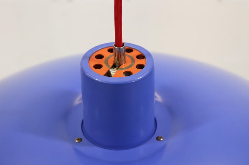Puede incluir: Una moderna l&aacute;mpara colgante con una pantalla azul y una carcasa cil&iacute;ndrica azul. La l&aacute;mpara tiene un interior naranja y un cable de alimentaci&oacute;n rojo. La luz est&aacute; suspendida del techo.