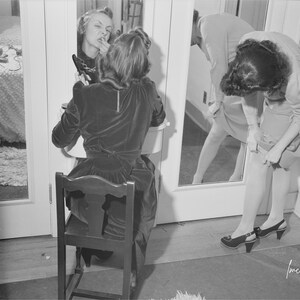 Girl putting on lipstick and another girl straightening seams in her stocking 1940s Photo Print