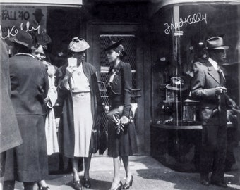 May include: Black and white photo of a group of people standing in front of a store called "Fred Kelly Hats". The store has a sign that says "Fall '40".