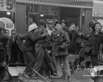 May include: A black and white photo of a group of children playing with toy wagons in front of a store. The store has signs advertising beans, grapefruit, and catsup. The children are wearing coats and hats.