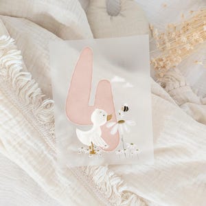 May include: A rectangular translucent card featuring a large, soft pink number four. A white duckling stands among small white daisies, looking toward a small bee hovering near a larger daisy. Two small white clouds are positioned above the duckling.