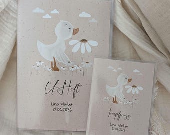 Puede incluir: Dos fundas protectoras beige para documentos, una etiquetada como U-Heft y la otra como Impfpass. Ambas presentan una ilustración de un pato blanco, margaritas y nubes. El texto Lina Winter y 12.06.2026 está impreso en cada funda en negro.