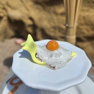 May include: A white ceramic mug with a black handle and the text "But First, Coffee" in a bold, black font. The mug is set against a blurred background, suggesting a cozy setting. The mug appears to be approximately 4 inches tall.