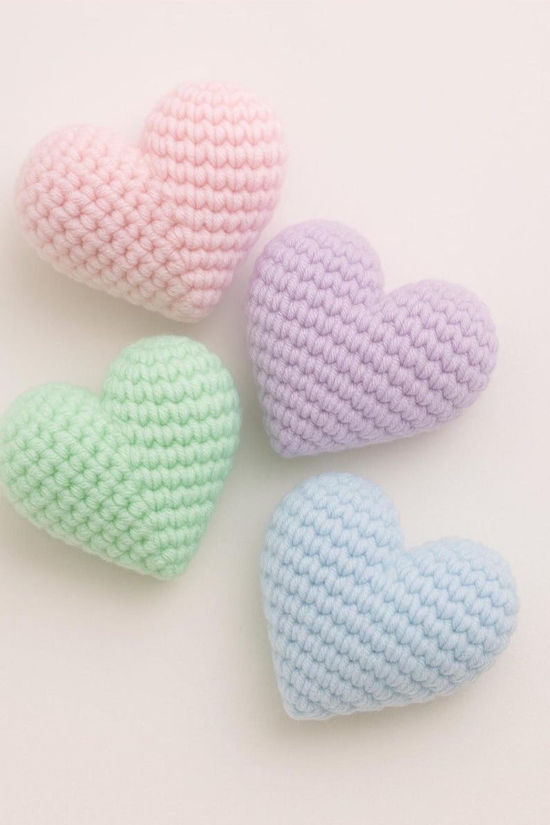 May include: Four handmade crochet hearts in pastel colors: pink, lavender, green, and blue. Each heart is crafted with a textured stitch, creating a soft, plush appearance. The hearts are arranged on a white background, perfect for Valentine's Day or other celebrations.