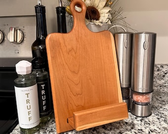 May include: A wooden cutting board with a handle and a stand, alongside bottles of truffle oil and black bottles with silver spouts. Two stainless steel salt and pepper grinders are also visible.