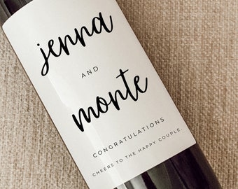 May include: A white wine bottle label with black text that reads "jenna and monte" with the words "Congratulations" and "Cheers to the happy couple" below. The label is 4 inches by 5 inches and is waterproof, repositionable, and removable.