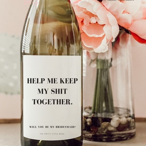 May include: A white wine bottle with a white label that says "Help me keep my shit together. Will you be my bridesmaid? The Pretty Little Mess".