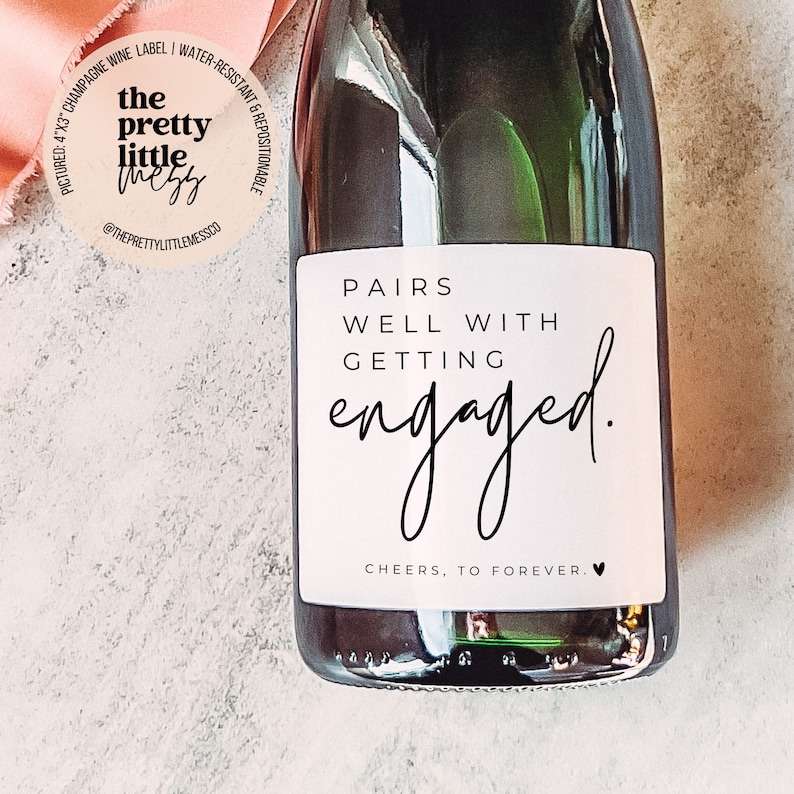 Puede incluir: Etiqueta de botella de champ&aacute;n con fondo blanco y texto negro que dice "Pairs well with getting engaged. Cheers, to forever."