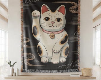 May include: A black and white tapestry featuring a cartoon image of a white cat with black spots, holding up its right paw. The cat is wearing a pink collar with a gold bell. The background is black with white clouds and swirls.