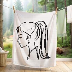 May include: White towel with a black pixelated illustration of a woman's profile with a ponytail and a star-shaped earring. The towel is hanging on a clothesline with a wooden clothespin. Other towels are hanging in the background.