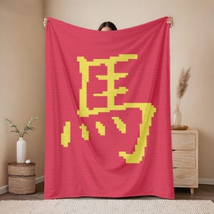 Könnte beinhalten: Eine rote Decke mit einem großen gelben chinesischen Schriftzeichen. Die Decke wird präsentiert und hebt die kühne Grafik vor einem einfarbigen roten Hintergrund hervor. Das Design ist pixelig und bietet eine moderne Ästhetik.