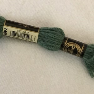 Könnte beinhalten: Ein Knäuel DMC Stickgarn in grüner Farbe. Das Etikett trägt die Aufschrift "DMC" und "LOT 24222" mit einem Barcode. Das Knäuel ist mit der Nummer "7406" gekennzeichnet.