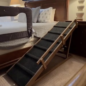 May include: A wooden pet ramp with a dark gray carpet surface and a wooden handrail. The ramp is angled and has a brown wooden base.
