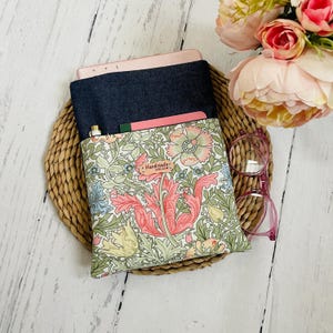 May include: A white and green floral patterned fabric book sleeve with a denim flap and a pink pocket. The sleeve has a small label that says "Handmade with Love".