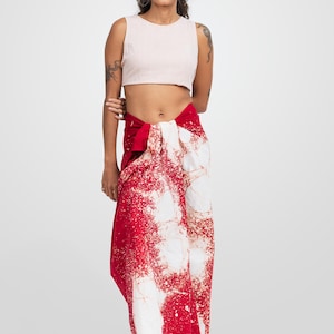 以下が含まれることがあります： 明るいピンク色のクロップトップと、赤と白の模様のサロン。 サロンは大胆で抽象的なデザインが特徴です。 この衣装はスタイリッシュなアンサンブルで、暖かい季節やビーチでの外出に最適です。