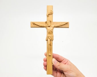 May include: A wooden crucifix with a carved figure of Jesus Christ. The crucifix is held in a hand against a white background.