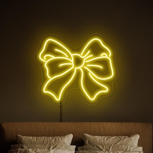Op de afbeelding: Een gele neon boogvormige lichtarmatuur is boven een bed met wit beddengoed en een bruine deken gemonteerd. Het neonbord is een decoratief element en geeft de kamer een warme gloed. De muur is donkerbruin.
