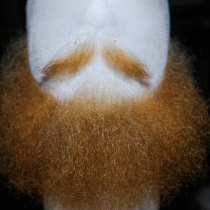 May include: A close-up of a fake beard with a mustache. The beard is made of brown and orange hair and is very full. The mustache is also brown and orange and is neatly trimmed.