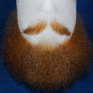 May include: A close-up of a red beard on a mannequin head. The beard is thick and full, with a slight mustache.