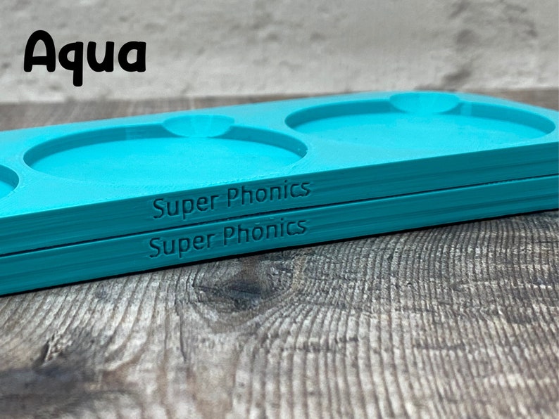 Pu&ograve; includere: Due vassoi in plastica blu turchese con tre incavi circolari. I vassoi sono impilati uno sopra l'altro. Il testo "Super Phonics" &egrave; stampato sul fondo di ogni vassoio.