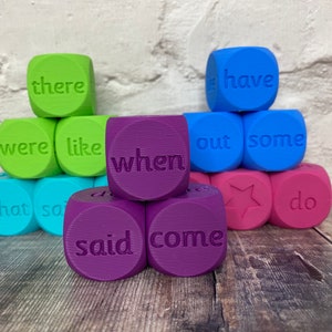 May include: A set of colourful dice with different words printed on each side. The words include "there", "were", "like", "what", "said", "come", "when", "have", "out", "some", "do".