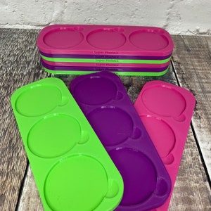 Pu&ograve; includere: Tre stampi in silicone per realizzare oggetti rotondi in resina. Gli stampi sono verdi, viola e rosa. Ogni stampo ha tre cavit&agrave; rotonde. Gli stampi sono impilati uno sopra l'altro.