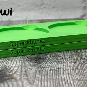 Pu&ograve; includere: Due vassoi di plastica verde con le parole "Super Phonics" stampate sul fondo. I vassoi hanno tre rientranze circolari.