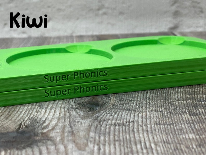 Pu&ograve; includere: Due vassoi di plastica verde con le parole "Super Phonics" stampate sul fondo. I vassoi hanno tre rientranze circolari.