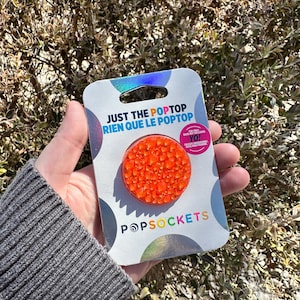 May include: Orange PopSocket phone grip with a sparkly finish. The packaging says "Just the PopTop Rien que le PopTop" and features the PopSocket logo.
