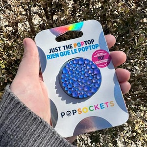May include: A blue PopSocket phone grip with a sparkly, iridescent finish. The packaging says "Just the PopTop Rien que le PopTop" and features the PopSockets logo.
