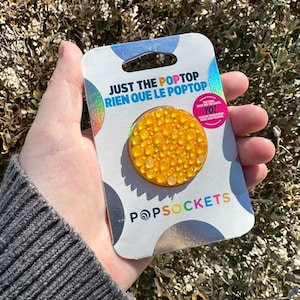 May include: A yellow PopSocket phone grip with a sparkly finish. The packaging says "Just the PopTop Rien que le PopTop" and features the PopSockets logo.