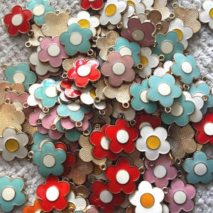 May include: A collection of colorful flower-shaped charms in various colors, including red, pink, blue, and white, with gold-colored metal accents. The charms have a glossy finish and are suitable for jewelry making or craft projects.