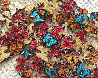 May include: A collection of colorful butterfly charms. The charms feature gold-colored metal wings and bodies, with vibrant enamel in shades of red, orange, blue, and gold. The butterflies are arranged closely together, creating a visually appealing display.