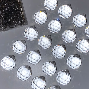 Peut inclure: Une collection de 18 boules facettées en cristal transparent, disposées en forme de triangle sur une surface grise.