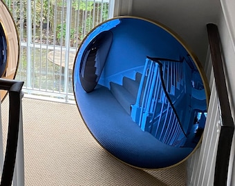 Pode incluir: Dois espelhos redondos, um dourado e outro azul, estão pendurados em uma parede de um corredor. Os espelhos refletem a escada e a janela atrás deles.