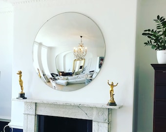 Pode incluir: Uma lareira branca com uma moldura de mármore e uma lareira preta. A lareira é decorada com um grande espelho redondo e duas estátuas douradas. Há uma pilha de lenha na lareira.