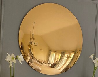 May include: A large, round, gold-colored mirror hangs on a gray wall above a white, ornately carved fireplace mantel. Two white amaryllis flowers are in silver vases on either side of the mantel.
