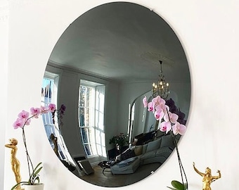 May include: A large, round, black mirror with a slightly convex surface reflects a room with a window and a chandelier. The mirror is hanging on a white wall.