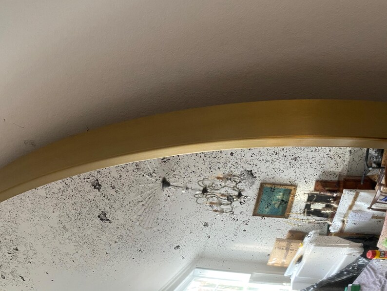 Pode incluir: Um espelho grande, redondo, com moldura dourada e superf&iacute;cie branca desgastada. O espelho reflete uma sala com um candelabro, uma pintura e outros m&oacute;veis.